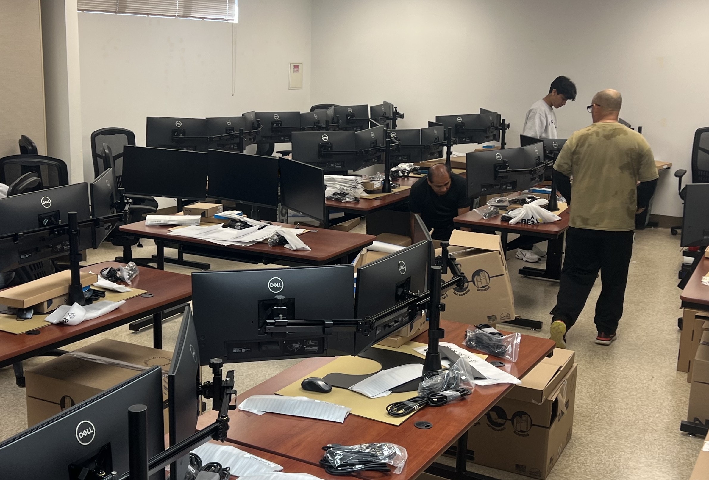 JIRACOR personnel performing large-scale training system technical refresh, installing Dell workstations and dual-monitor assemblies across a full classroom of operator stations
